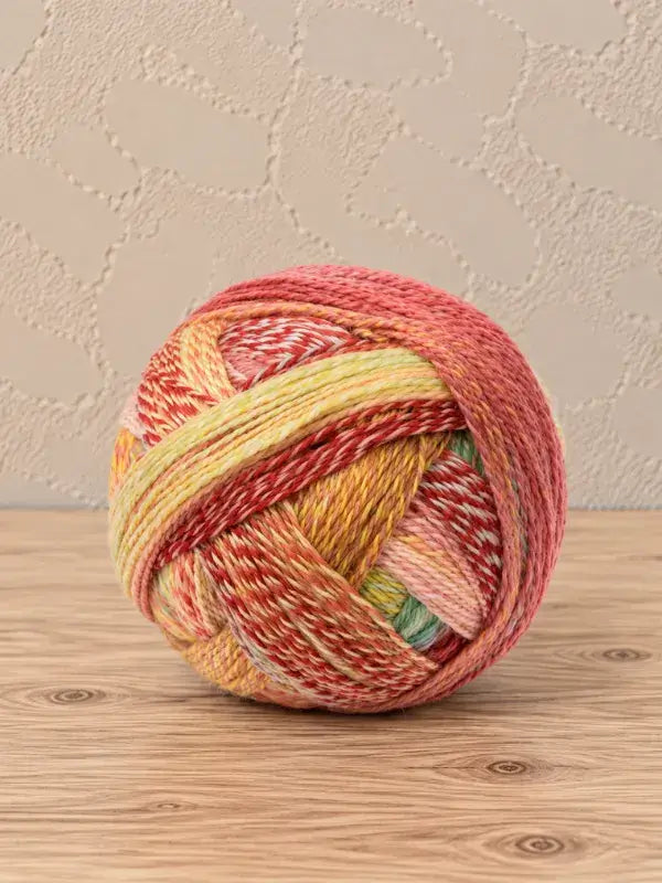 A ball of Schoppel wolle Zauberball crazy yarn featuring multicolored, variegated sections of coral, yellow, and green.