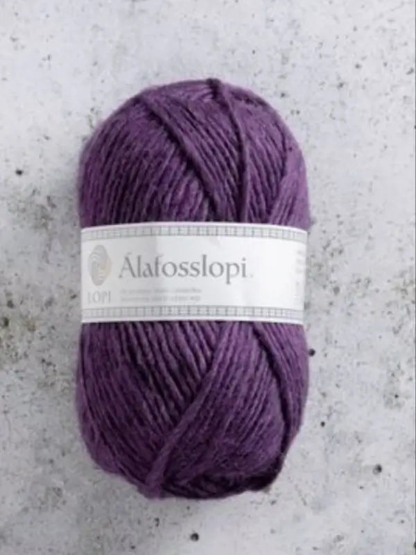 A skein of purple Istex Alafosslopi yarn, a renowned islantilainen villalanka, with a white label rests on a light gray, speckled surface.